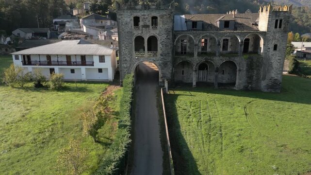 Arched gateway and stone towers of the Castle of Arnado front a long driveway and green lawn, aerial