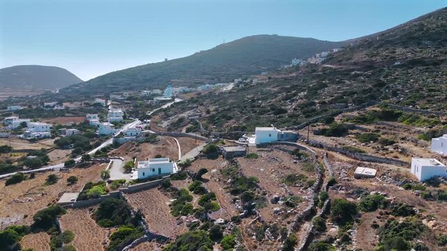 Aerial drone shot of the whitewashed village of Arkesini with a blue-domed church and scattered houses on an arid terraced hillside in Kato Meria, southern Amorgos, Cyclades, Greece