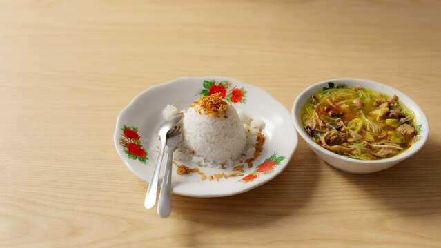 Traditional Indonesian soto padang beef soup served with steamed rice topped with crispy fried shallots on a wooden table, perfect for Asian restaurant menu.