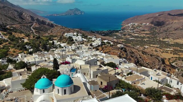 Aerial drone shot flying close over the blue domes of the church of Agioi Anargyroi among the white houses of Tholaria above Aegiali on Amorgos, Cyclades, Greece