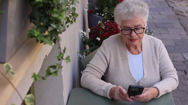 Senior woman making video call on smartphone at outdoor cafe. Digital communication, senior technology, social connection, active aging and staying connected concept