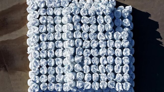 Aerial view of a large grid of white plastic-wrapped agricultural bales stored on a farm in Eleja, Jelgava Municipality, Latvia.
