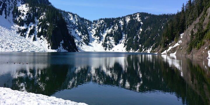 Calm lake reflecting snow-capped mountains and evergreen forest