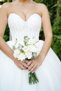Bride holding a small white wedding bouquet with eucalyptus in front of a beaded corset dress, close up