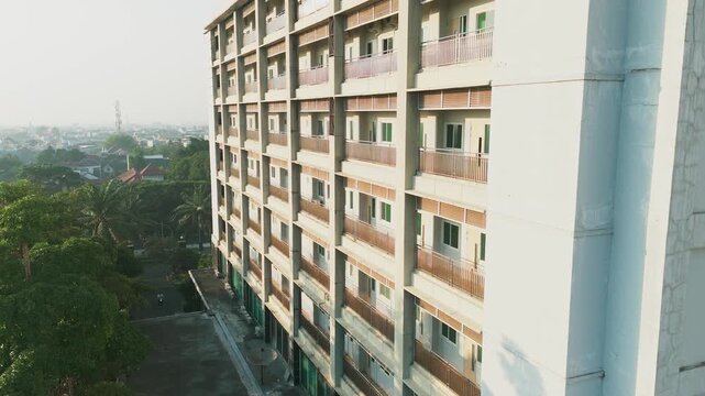 Aerial view of a modern multi-story apartment building with concrete balconies and grid facade in the urban landscape of Malang, East Java, Indonesia.