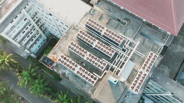Aerial view of multiple industrial air conditioning units installed on a concrete rooftop with visible piping and surrounding palm trees in Malang, East Java, Indonesia.