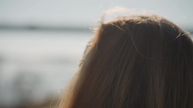 Woman with long hair is seen from behind and side angles looking out over body of water. Her profile remains consistent as camera angle shifts slightly throughout scene capturing soft