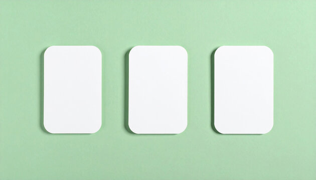 Top-down view of three blank rounded-corner cards on pastel green surface, clean minimalist composition, white card stock, evenly spaced layout, modern stationery mockup. Close-up.