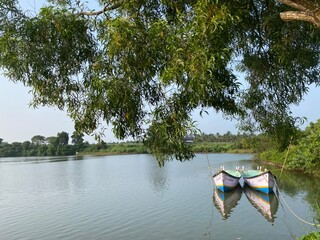 Two colorful fishing boats anchored on calm lake water with tree branches overhead reflection in coastal Karnataka India © Ganesh
