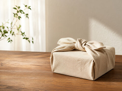 A beige gift box rests on a dark brown wooden table, tied with a natural fabric knot.