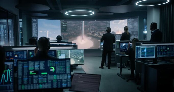 Monitoring Control Room. Team of Engineers in Headsets Track Telemetry on Multi-screen Workstations While a Large Display Shows a Rocket Booster Landing During a Successful Space Mission Launch