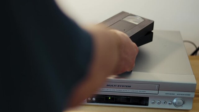Man hand picking up and inserting cassette into vintage VCR