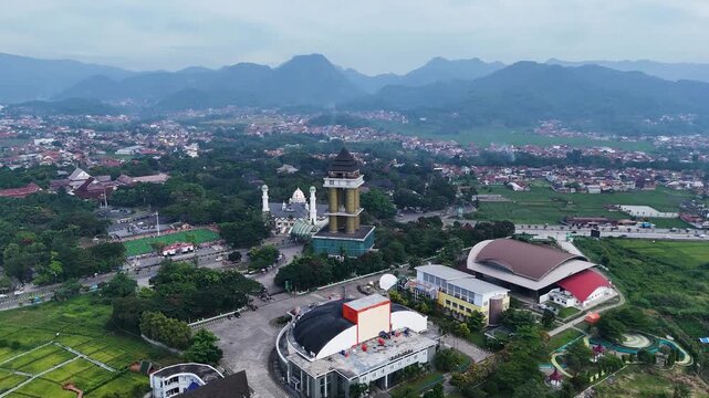Aerial view of Soreang tower, mosque, and modern buildings surrounded by lush green fields and mountains in Bandung, West Java, Indonesia.