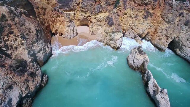 Dramatic aerial view flying over a small secret beach hidden amongst the stunning limestone cliffs and sea stacks of praia do alemao in portimao, a famous algarve vacation spot in portugal