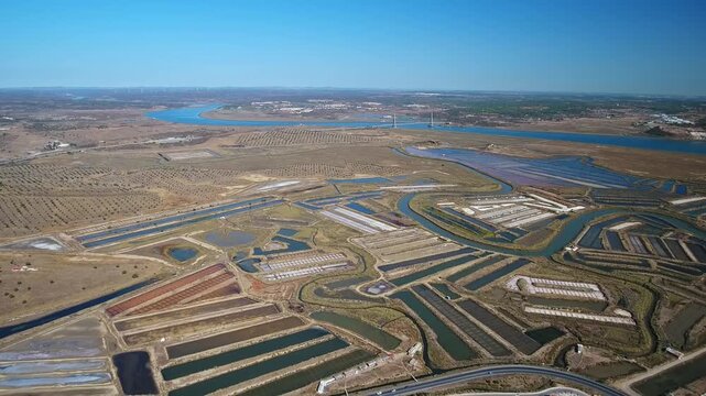 Aerial drone footage flying backwards over the traditional salt pans and evaporation ponds of castro marim in algarve, portugal, revealing the guadiana river and the spanish border