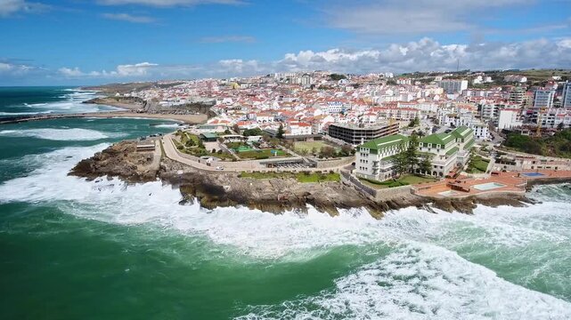 Dramatic aerial perspective of powerful atlantic ocean waves crashing against the rocky coastline of ericeira, a picturesque surfing village in portugal, on a sunny day with blue skies