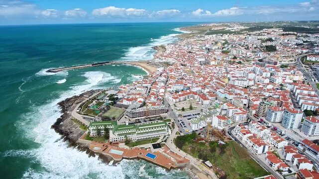 Beautiful aerial perspective of ericeira, a charming seaside town in portugal, showing the traditional houses with red roofs and the powerful atlantic ocean waves crashing against the rocky coast