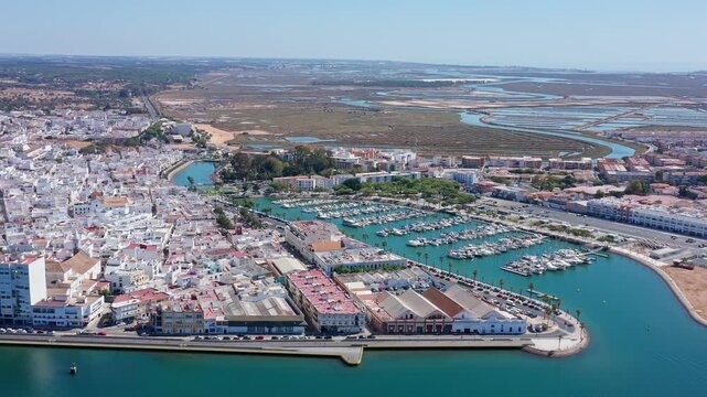 Expansive aerial view showcasing the charming whitewashed town of ayamonte, its bustling marina filled with boats, and the scenic guadiana river estuary under a clear sunny sky in spain