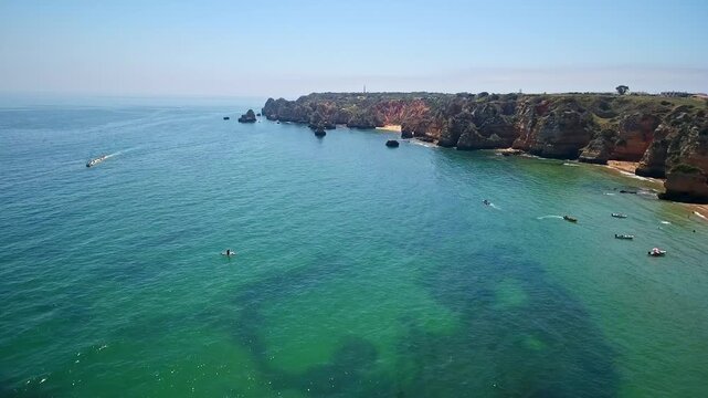 Stunning panoramic view of the turquoise ocean, picturesque cliffs, and sandy shores of camilo beach in lagos, algarve, portugal, with tourist boats sailing near the impressive coastline