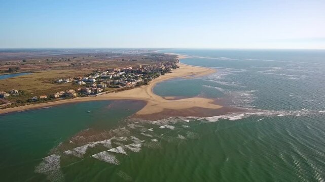 Scenic aerial footage showing the beautiful isla canela coastline in ayamonte, spain, with the green ocean waters meeting the sandy beach and the town in the background on a sunny day