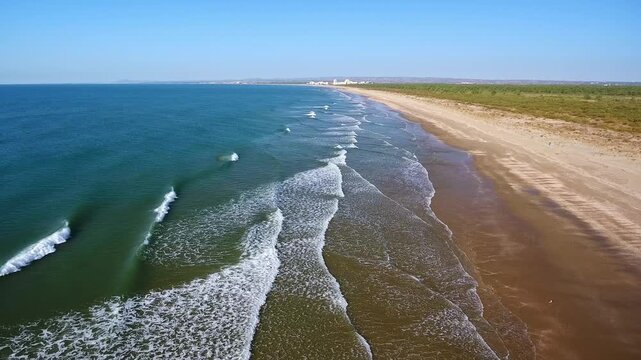 Majestic aerial view showing turquoise ocean waves breaking along a deserted sandy beach on a sunny day, creating a mesmerizing natural pattern with white foam against the golden shore