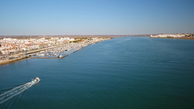 Aerial view of a fishing boat leaving the beautiful marina of vila real de santo antonio, in algarve, portugal, with the guadiana river and the town of ayamonte, spain, in the distance