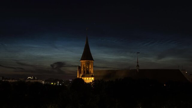 Night to morning time lapse of illuminated gothic cathedral spire against dark blue sky and pre-dawn sunrise glow