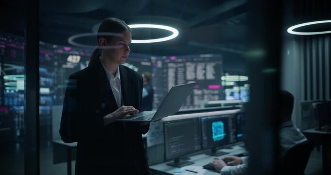 Quantitative Analyst Working on a Laptop to Boost Ecommerce Conversion and Payment Flows While Male Specialists Track Neural Network, Freight and Threat Defence Walls in a Big Data Command Centre.
