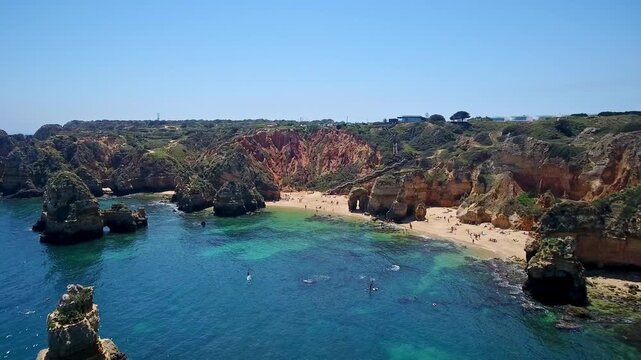 Aerial view of the stunning camilo beach in lagos, algarve region, portugal. Tourists are relaxing on the golden sand and swimming in the clear turquoise atlantic ocean water among rock formations