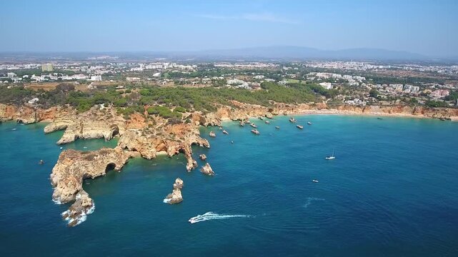 Stunning aerial perspective showing the beautiful coastline of portimao, portugal, with rugged cliffs, golden beaches, and boats sailing on the turquoise atlantic ocean under a clear blue sky