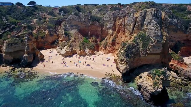Stunning aerial view of people sunbathing and swimming at praia do camilo in lagos, algarve, a picturesque travel destination with golden cliffs, turquoise water, and sandy coves