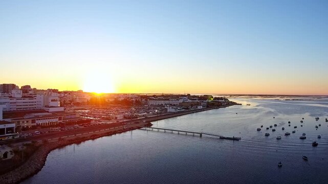 Gorgeous aerial view flying over the scenic coastal city of faro, portugal, during a breathtaking sunrise, revealing the tranquil marina, the calm sea, and the glowing city skyline