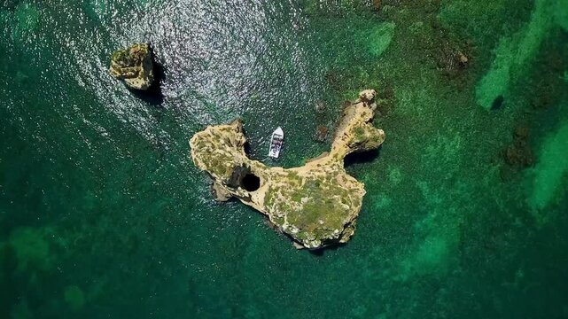 Majestic aerial top down view of a small tour boat navigating the emerald green waters around the stunning limestone rock formations of ponta da piedade near lagos in the algarve, portugal