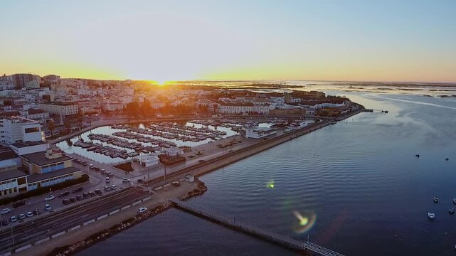Aerial cityscape of faro, portugal showing the marina with moored boats and the old town reflecting the beautiful golden light of a calm sunrise over the ria formosa lagoon in the algarve region