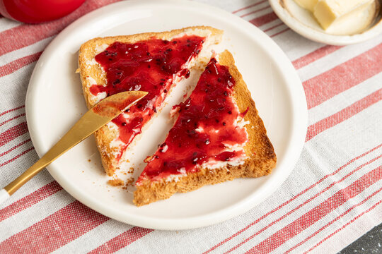 Close up of toasted bread slice cut in half and spread with butter and sweet red gooseberry jam