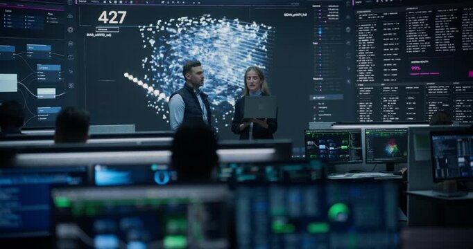 Portrait of a Financial Risk Analyst and an E-commerce Logistics Manager Holding a Laptop, Discussing AI Network Insights on a Big Screen in Statistics Monitoring Room Improving Payment Security.