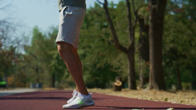 A young man performs a dynamic jumping exercise on a red track in a sunny park. He engages in an outdoor fitness routine, focusing on agile footwork.