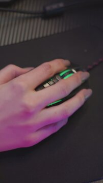 Hand with painted nails rests on black mouse moving slightly to interact. scene features soft purple and green lighting effects over skin tone of arm and background elements like fabric