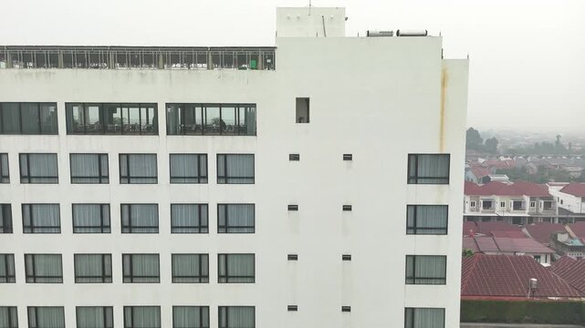 The apartment building&rsquo;s white facade features a row of uniform windows and a rooftop terrace overlooking the misty suburban cityscape.