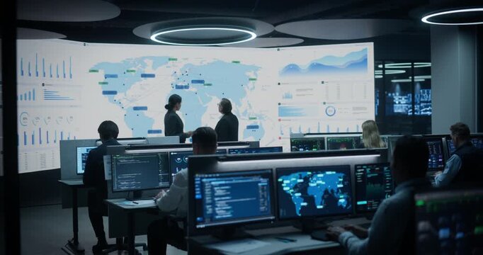 Operations Manager Points at Global Map Trade Routes While Data Science Lead Listens to Strategy Talk in Analytics Control Center, Specialists Monitor Payments, Logistics Cargo and Cybersecurity 