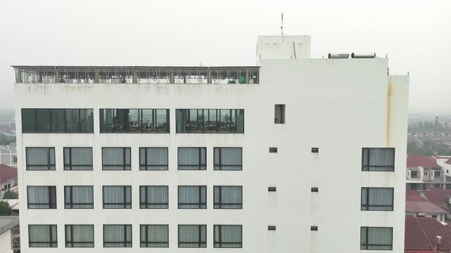 The apartment building&rsquo;s white facade features a row of uniform windows and a rooftop terrace overlooking the misty suburban cityscape.