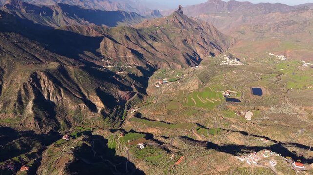 Drone flight over the Caldera de Tejeda in Gran Canaria, with Roque Bentayga rising above green terraces, small villages, winding roads and reservoirs.