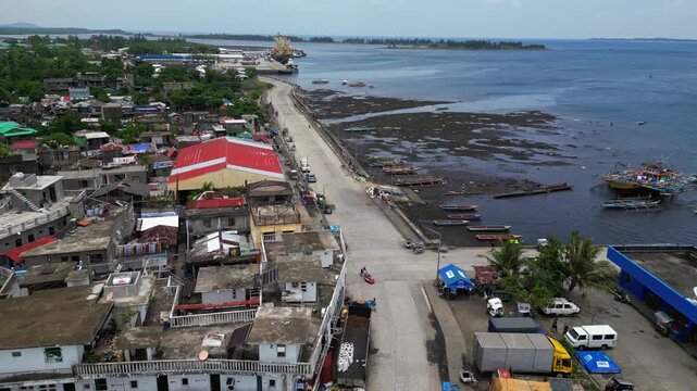 Aerial drone footage of San Roque Boulevard and the waterfront near Tabaco Port in Tabaco City, Albay, Philippines. View of the coastal road, port area, boats and urban shoreline under clear sunny ski