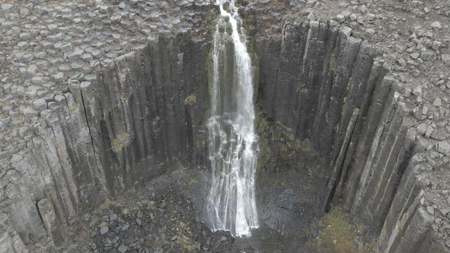 Aerial view of Litlanesfoss waterfall cascading over hexagonal basalt columns in Iceland.
