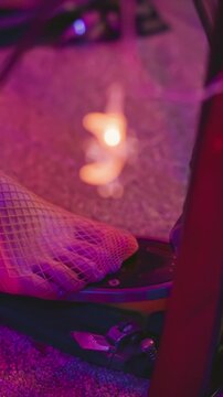 Foot in fishnet stocking presses pedal under purple and pink stage lighting with soft focus on mesh texture and carpet background. scene emphasizes close up details of movement within indoor