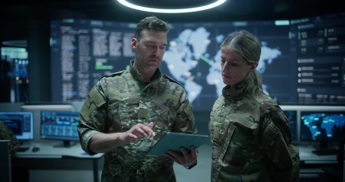 Army Base Military Surveillance Monitoring Control Room: Male and Female Soldiers Hold a Meeting and Talk Over a Tablet Computer, Reviewing Ai Reconnaissance Data While Analysts Track Threats