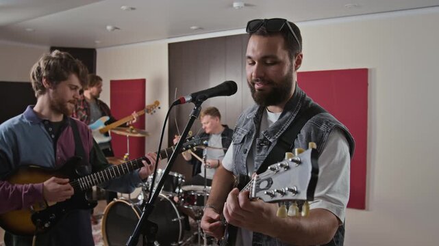 Young adult Caucasian musicians rehearsing song in music studio, playing electric guitars and drums. Footage ideal for entertainment advertising, music education, and band promo videos