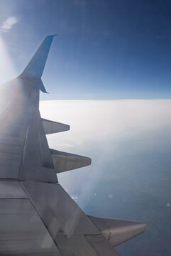 Passenger airplane aircraft wing with blue winglet flying high above the earth ground during a scenic sunset evening sky. Modern commercial aviation transport vehicle, summer vacation journey. 