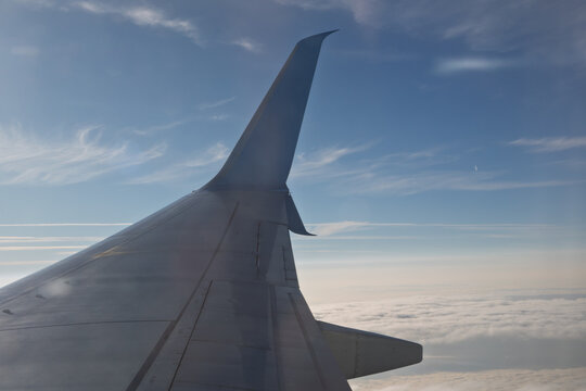 Passenger airplane aircraft wing with blue winglet flying high above the earth ground during a scenic sunset evening sky. Modern commercial aviation transport vehicle, summer vacation journey. 