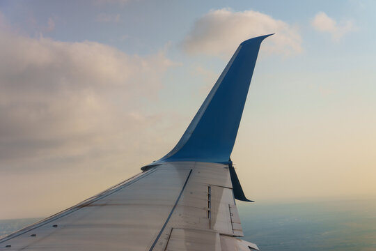 Passenger airplane aircraft wing with blue winglet flying high above the earth ground during a scenic sunset evening sky. Modern commercial aviation transport vehicle, summer vacation journey. 